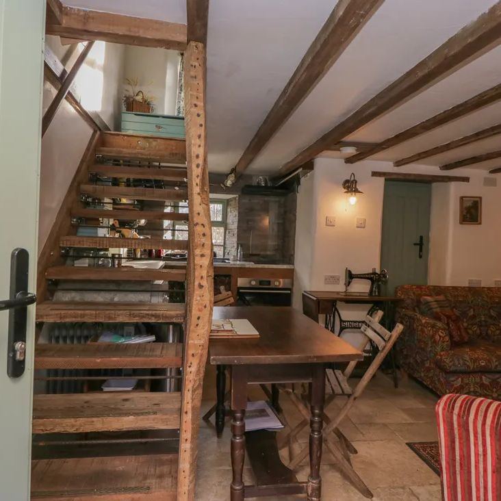 The open-plan living area at The Old Cart House with a steep wooden staircase, dining table and patterned sofa