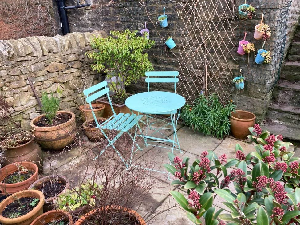 A small outdoor patio with a blue metal table and two chairs surrounded by potted plants at The Old Cart House in Garsdale near Sedbergh