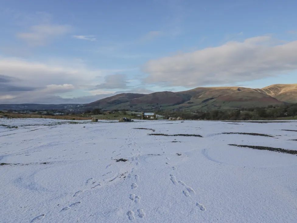 A snowy field with footprints leading to a gate and hills in the background at The Old Cart House in Garsdale near Sedbergh