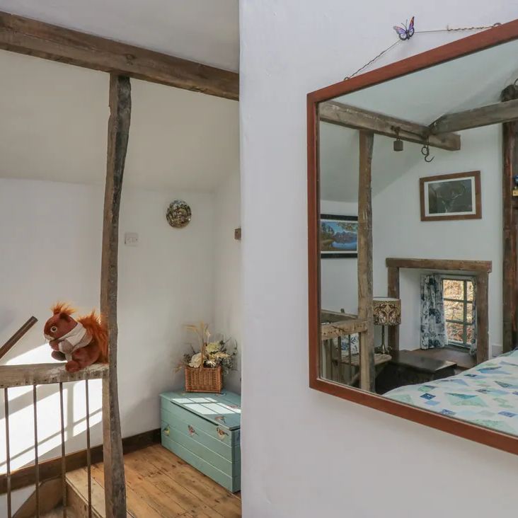 A cottage landing at The Old Cart House with a toy squirrel on the stair rail and a mirror reflecting the bedroom