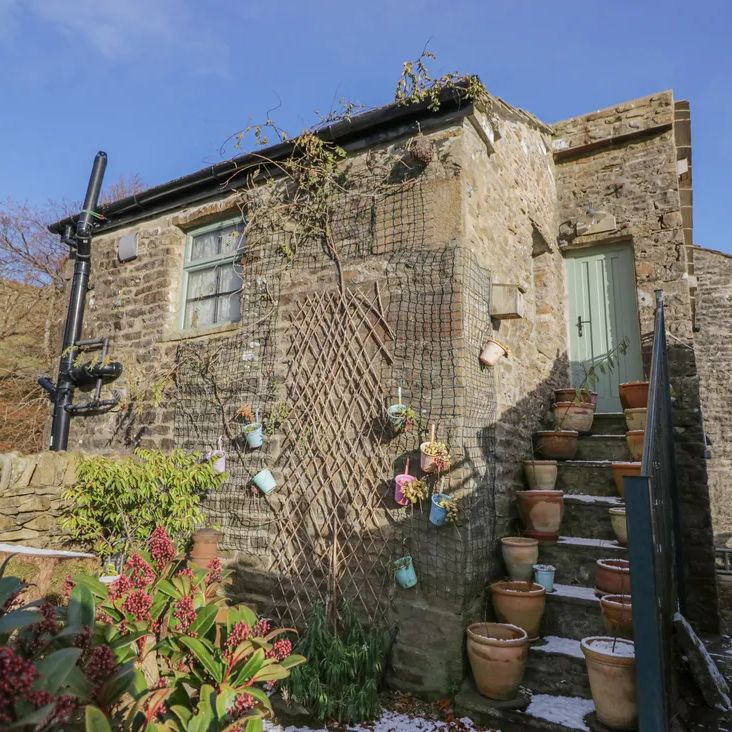 Stone steps lined with terracotta pots leading to the sage-green door of The Old Cart House on a snowy day