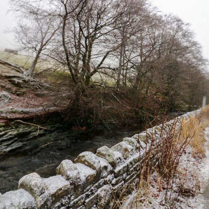 A snowy lane beside a dry-stone wall and a fast-flowing beck near The Old Cart House