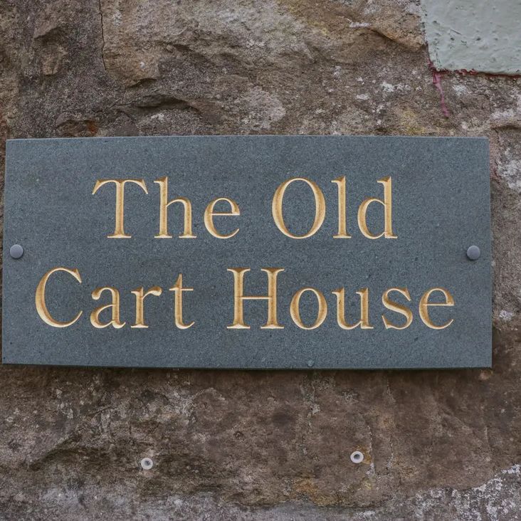 A slate plaque reading The Old Cart House in gold lettering, mounted on a stone wall
