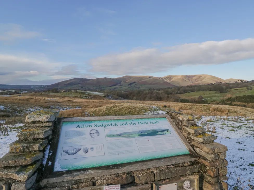 An outdoor information board about Adam Sedgwick and the Dent fault with hills and fields in the background at The Old Cart House in Garsdale near Sedbergh