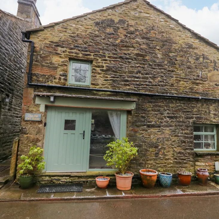 The stone exterior of The Old Cart House with its sage-green door and windows and a row of plant pots, in winter