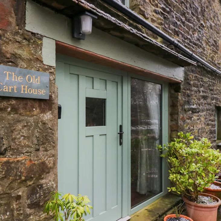 The sage-green entrance door and slate name plaque of The Old Cart House, with potted plants, on a frosty day