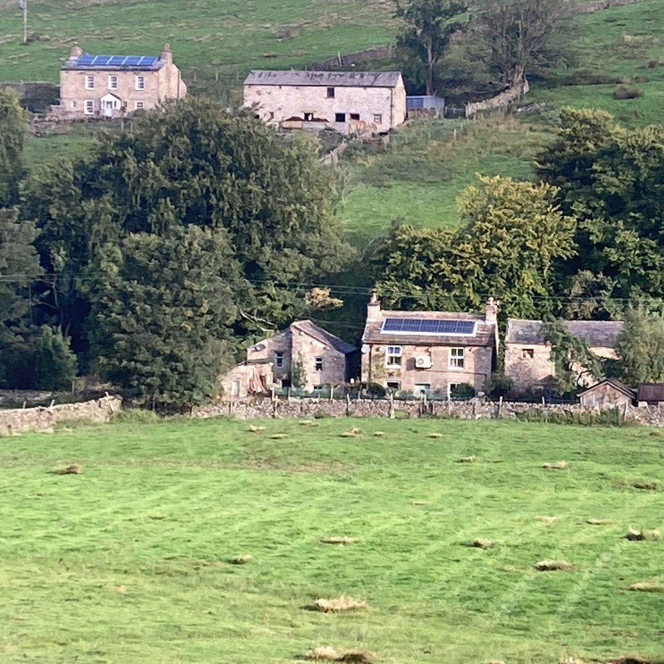 Stone cottages and barns with solar panels among green fields and dry-stone walls in a Garsdale valley