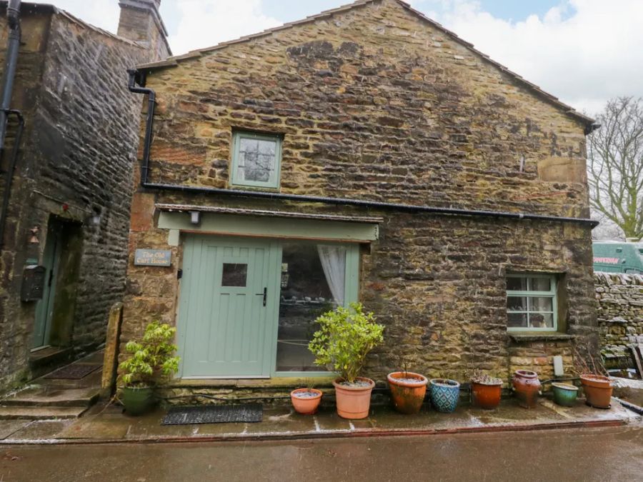 Stone exterior of a house with green door and windows and potted plants outside at The Old Cart House in Garsdale near Sedbergh